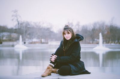 Young woman sitting on snow against lake during winter