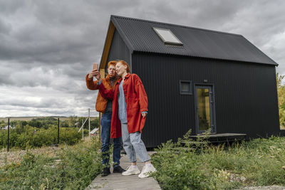 Young couple taking selfie standing in front of tiny house