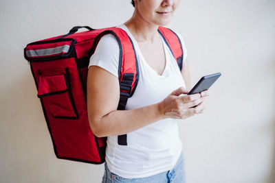 Midsection of young woman using phone while standing against wall