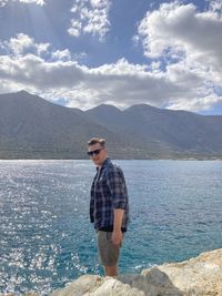 Young man standing in sea against mountains