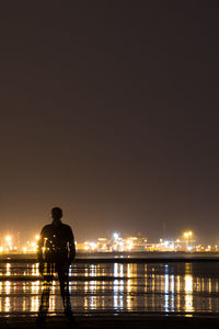 Man standing on illuminated bridge over river at night