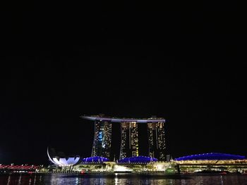 Illuminated ferris wheel in city against clear sky at night