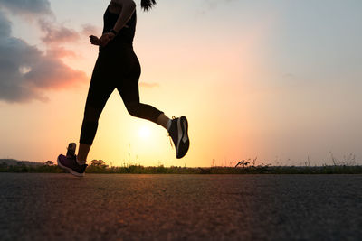 Low section of man jumping against sky during sunset