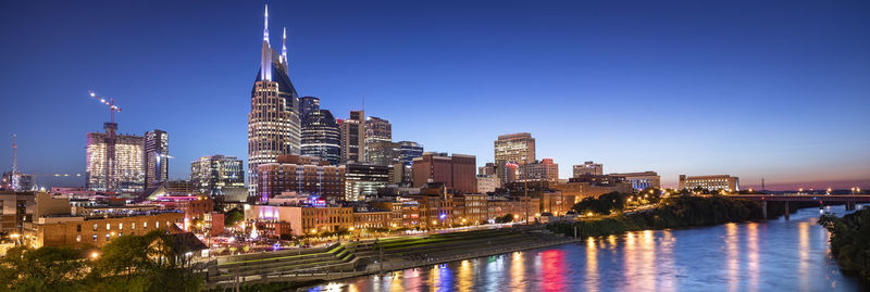 Illuminated buildings by river against sky at night