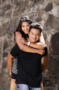 Portrait of smiling man piggybacking woman against wall