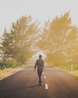 Rear angle view of young boy skateboarding on country road at sunset