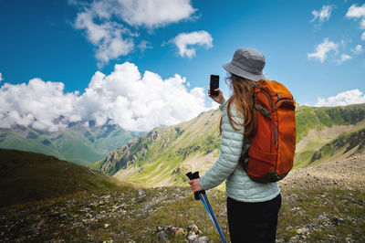 Beautiful young woman with blond hair photographs a mountain landscape on a phone camera while