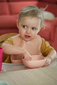 Toddler girl eating happily in high chair food by herself in the room. child having meal. happy kid