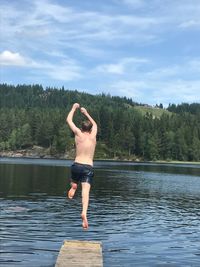 Rear view of shirtless man standing in lake against sky