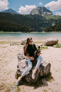 Full length of young woman sitting on rock by lake