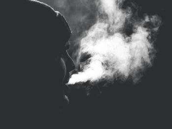 Close-up portrait of man smoking cigarette against black background