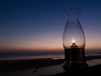 Close-up of illuminated lamp on beach against sky during sunset