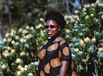 Smiling woman wearing sunglasses standing against plants