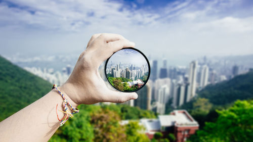 Close-up of hand holding camera against trees