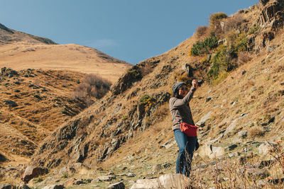 Rear view of man photographing on mountain against sky