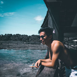 Portrait of smiling young man sitting on water against sky