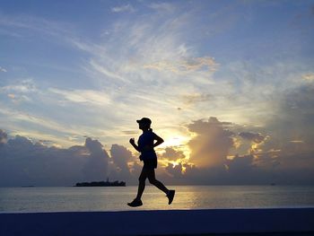 Silhouette woman on sea against sky during sunset