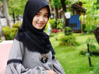 Portrait of smiling teenage girl wearing hijab while standing at back yard