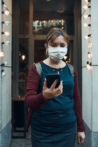 Young woman talking on phone standing in a front of restaurant downtown wearing the face mask