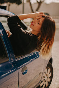 Young woman leaning through car window with closed eyes