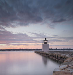 Lighthouse by sea against sky during sunset