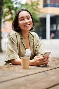 Young woman using mobile phone while sitting at table