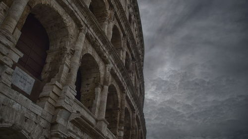 Low angle view of coliseum against cloudy sky