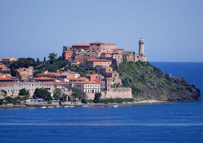 Buildings by sea against clear blue sky