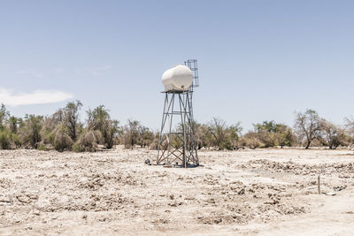 Water tower on land against sky during sunny day