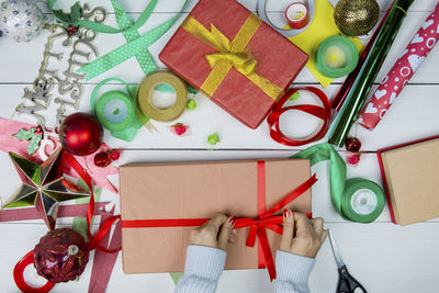 Cropped hand tying ribbon over christmas present with variety of decorations on table