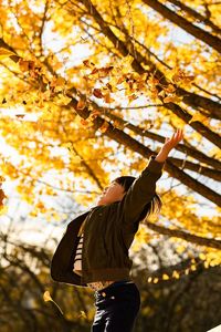 Side view of child with arms raised against autumn tree