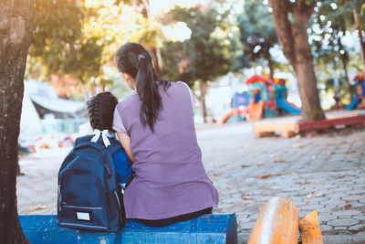Rear view of mother with daughter sitting on bench at playground