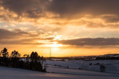 Snow covered landscape against sky during sunset