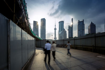 People walking on bridge against buildings in city