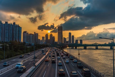 Vehicles on road amidst buildings against sky during sunset