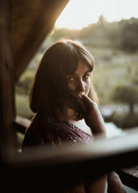 Portrait of young woman on ledge of wooden cabin at sunset