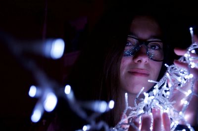 Portrait of young woman holding illuminated lighting equipment at night