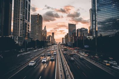 Vehicles on road amidst buildings in city during sunset