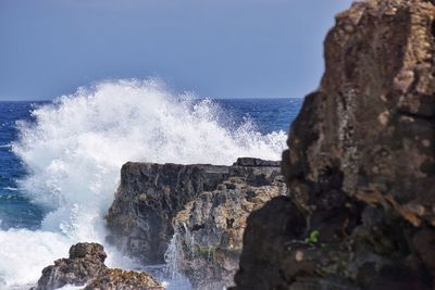 Waves splashing on rocks at shore against sky