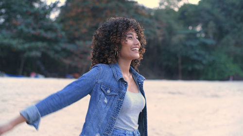 Happy young woman with curly hair standing at beach