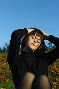 Portrait of young woman sitting on field against clear blue sky