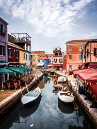 Boats moored in canal amidst buildings against sky