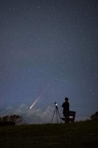 Rear view of man standing on field against sky at night