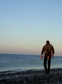 Rear view of man walking on beach against clear sky