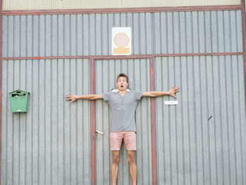 Portrait of shocked young man with arms outstretched against metallic door