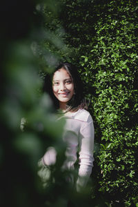 Portrait of smiling young woman standing against plants