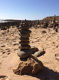 Stack of stones on sand at beach against clear sky
