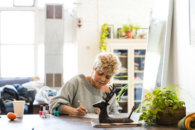 Mid adult woman writing at table while sitting in living room