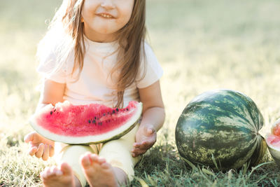 Cute baby girl 3-4 year old eating tasty watermelon over green nature background close up. 