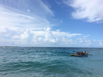 People rafting on sea against cloudy sky